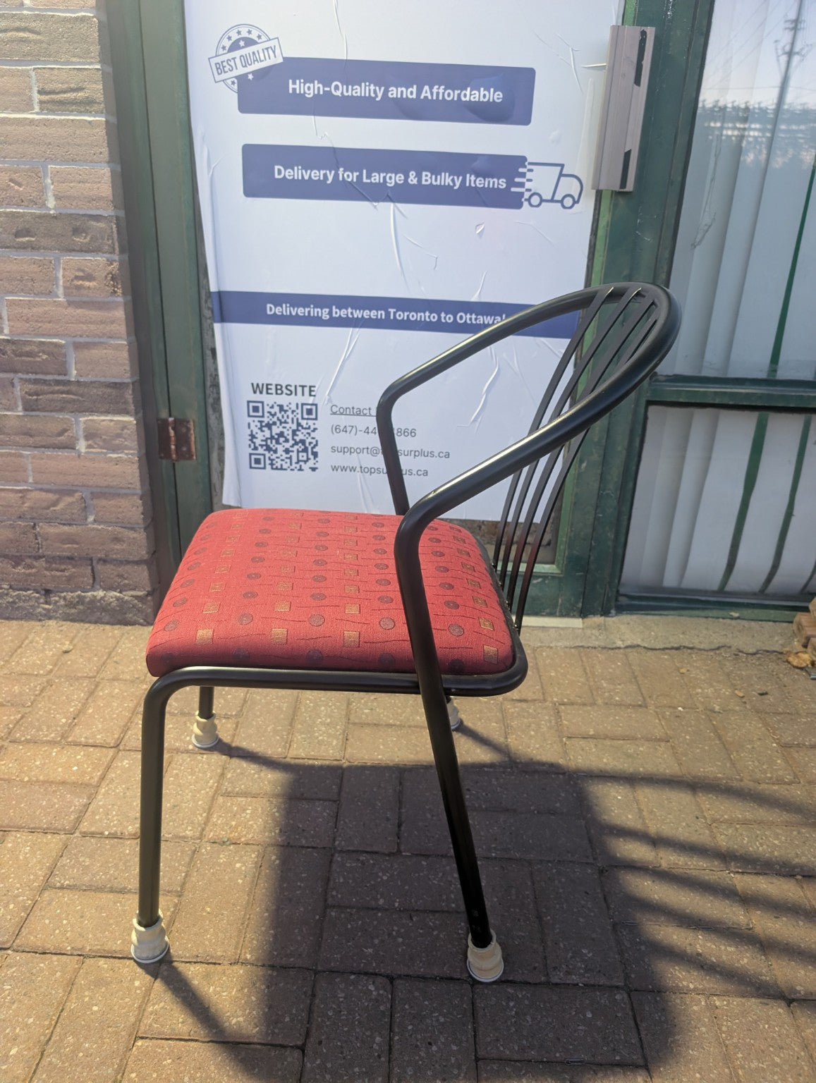 Red patterned upholstered stacking chair with black metal frame, side view