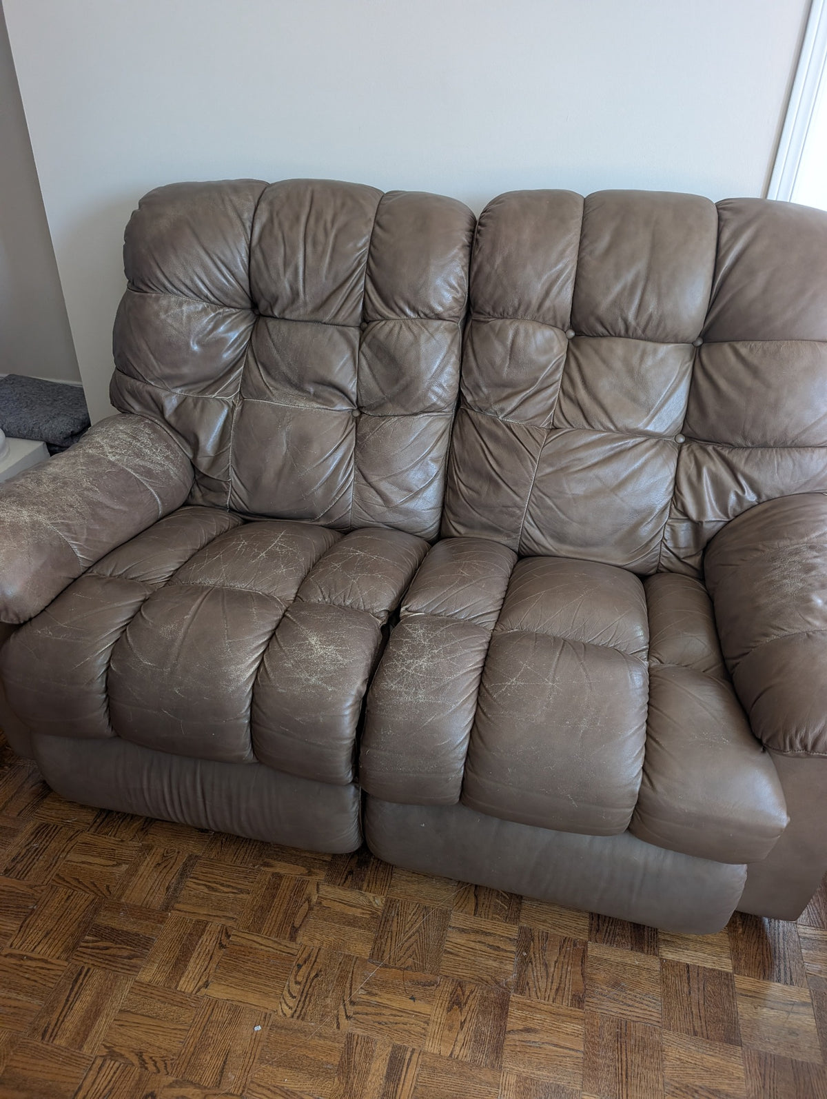 Taupe two-seat reclining sofa front view with visible upholstery wear